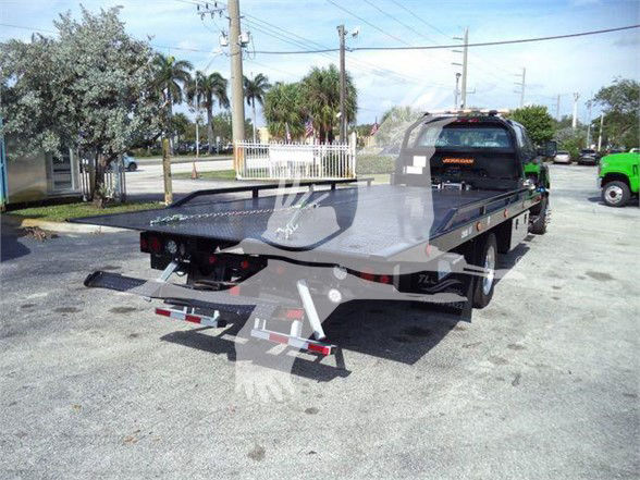 Tow truck flatbed with wheel lift; rear view showing flatbed and ramps, hitch, taillights, and decals.