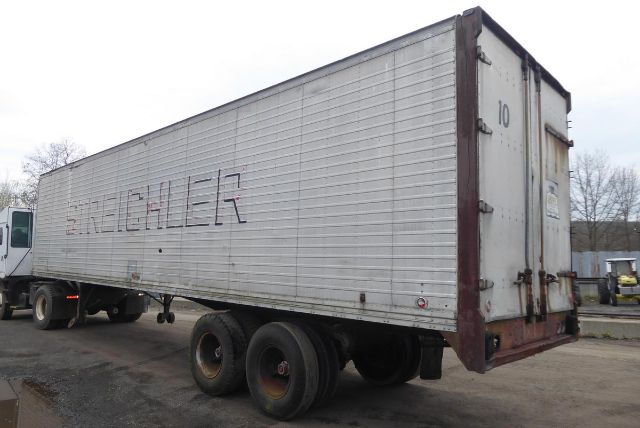 Trailer side view showing gooseneck? No, a long gray Sch? trailer with raised lettering 'BROWN' on the side; rear doors closed with number '10' on right door. Visible wheels and gravel lot.