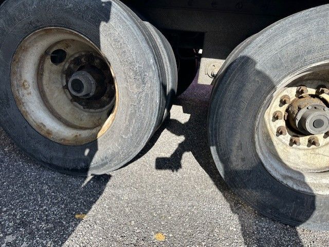 Two trailer wheels (dual axle) showing rims and hubs with lug nuts, on asphalt.