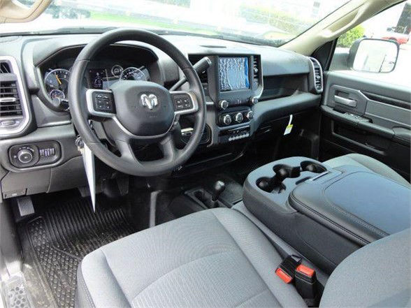 Ram pickup interior showing steering wheel with Ram emblem, center touchscreen, climate controls, gear shifter, and front seats.