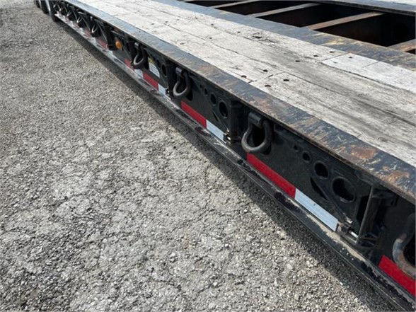 Side view of a Fontaine lowboy trailer frame with D-rings and reflective red/white tape along the edge.
