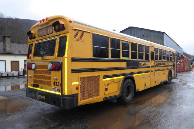 Vehicle side and rear view of a yellow Bluebird All American school bus with black stripes, numbered 455, in a yard.