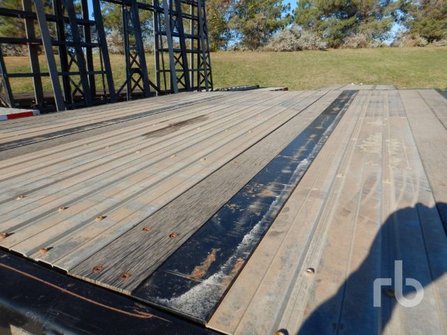 Flatbed trailer deck with metal planks, some painted darker strip in center, edge rails and shadows visible.