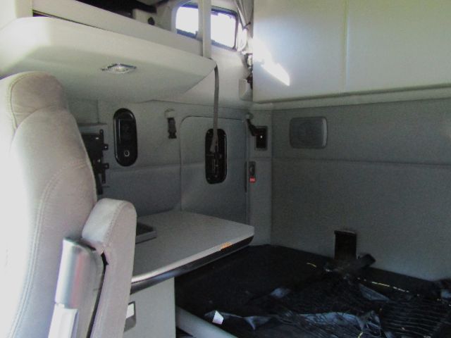 Interior of a 2020 Kenworth T680 cab and chassis showing driver's seat, storage shelf, and gray paneling.