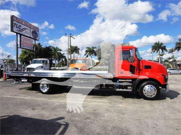 Mack MD6 tow truck with bright red cab and flatbed scene in a dealership lot.