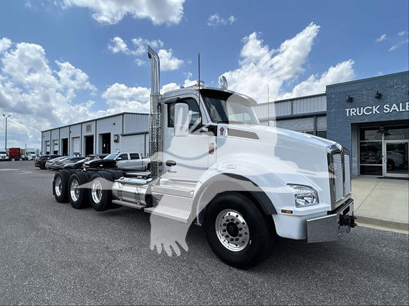 Kenworth T880 conventional daycab truck in a dealership lot, white finish with multiple axles, large chrome exhaust stack and grille.