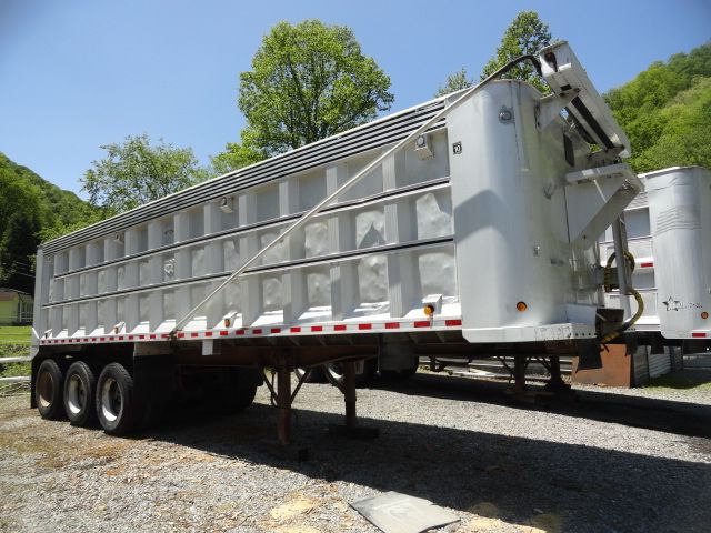1998 USTS 32ft steel dump trailer with triple-axle wheels and side panels. Front hydraulic tailgate and hitch visible.