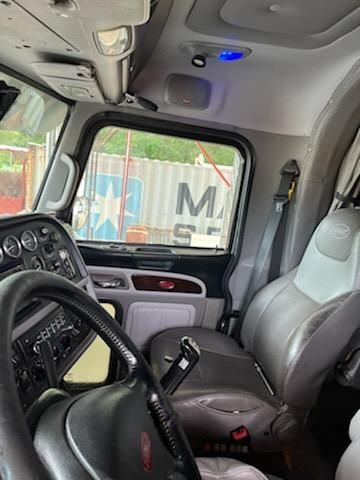 Interior view of a 2015 Peterbilt conventional sleeper truck cab showing steering wheel, dashboard with gauges, and two-tone gray seats.