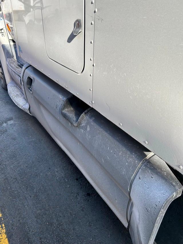 Peterbilt 579 side view with lower side skirt and riveted aluminum paneling; visible door edge and step, metallic gray exterior.