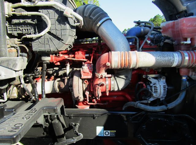 Kenworth T680 engine bay showing red engine block with large intake hoses and alternator, various hoses and wiring visible.