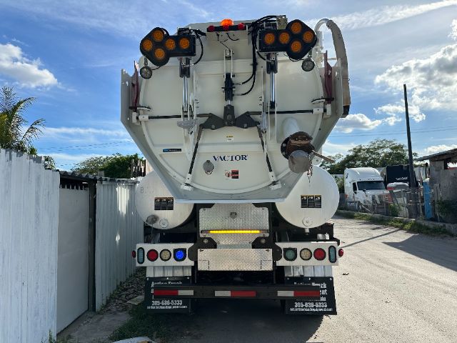 Rear view of a white vacuum truck with multiple circular red/amber warning lights, hoses, and equipment mounted on the back; vehicle branding 'VICTOR' visible on the rear hatch.