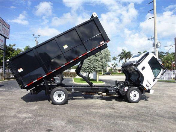 Isuzu NPR HD dump truck with a tilted black dump bed and white cab, chassis visible, side view.