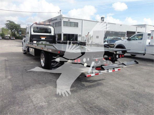 Tow truck flatbed rear view with heavy-duty wheel-lift and hydraulic bed, International MV model in background, dealership lot.