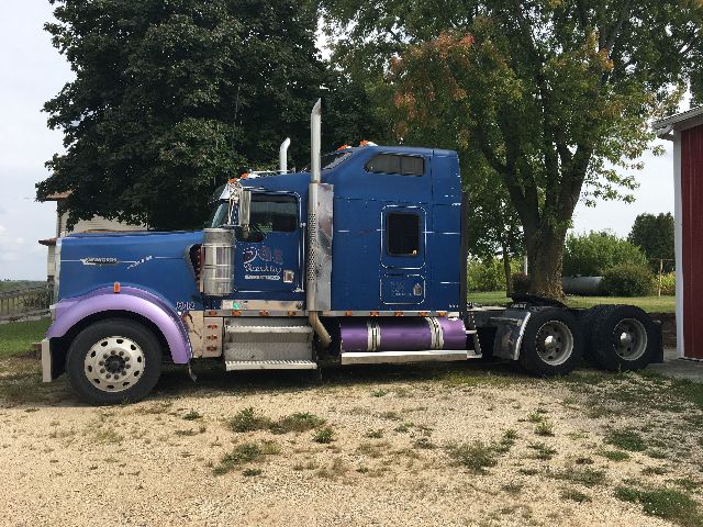 Kenworth W900L truck side view showing blue and purple color scheme and sleeper cab.