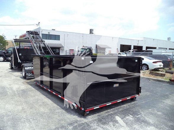 A black dump or flatbed trailer attached to a Chevrolet Silverado 6500HD truck in a dealership lot with a ladder rack and fencing in the background.