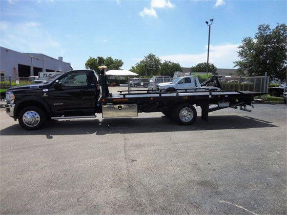 Black 2024 Ram 5500 SLT tow truck with long flatbed, side view showing cab and extended bed chassis.