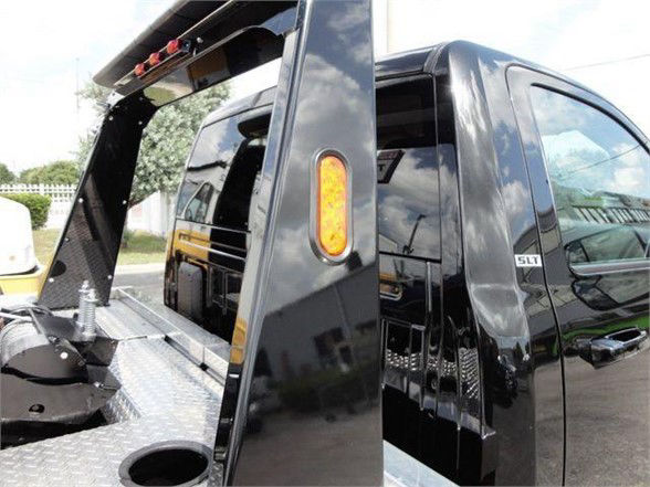 Ram 4500 HD SLT tow truck side view with hydraulic lift and flatbed platform. Visible: SLT badge on black crew cab, diamond plate metal bed, rear wheel well, orange side marker light.
