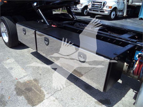 Peterbilt 337 truck bed with flat storage compartments and tools, visible hydraulic lines and part of cab in background.