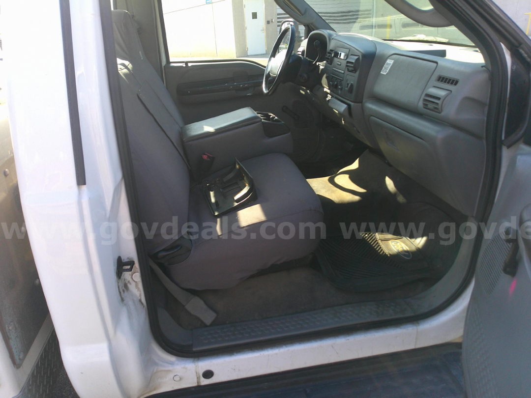 Interior of a Ford F-350 cab showing front seats, steering wheel, and dashboard from the driver’s side door. Gray upholstery and rubber floor mat visible.