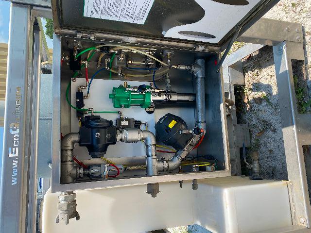 Trucking equipment cabinet open showing hydraulic/pump system with blue motor, green filter, various silver hydraulic lines and wiring.
