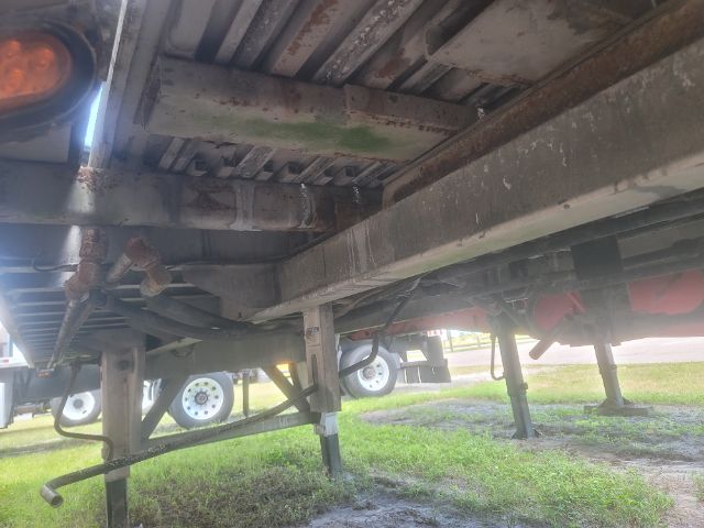 Underbelly of a walking floor trailer showing structural members, beams, hoses, and support legs.
