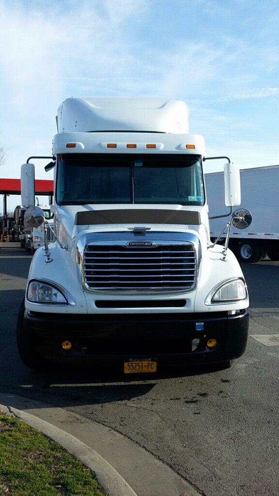 Truck front view of a white 2009 Freightliner Columbia conventional sleeper, with chrome grille, large side mirrors, and a yellow license plate.