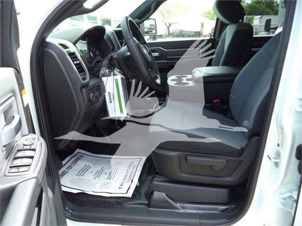 Truck interior driver's side with steering wheel, dashboard, and front seat; a paper mat on the floor and a dealership tag hanging from the dashboard.