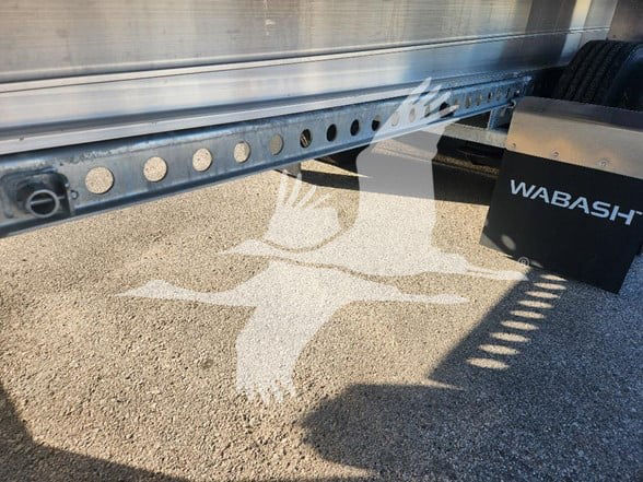 Trailer frame with perforated crossmember and wheel area; 'WABASH' branding on a black box near the ground.