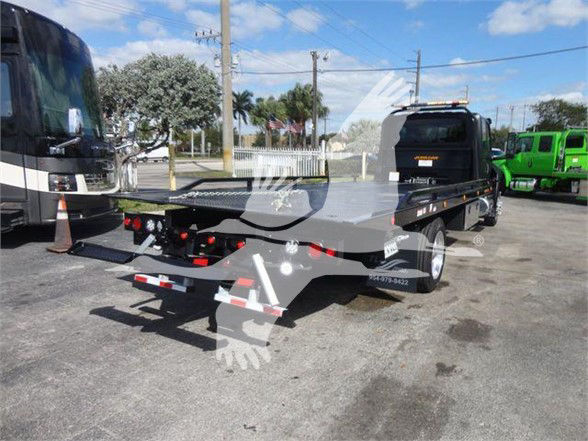 Flatbed tow truck rear view showing black metal deck, dual rear wheels, and towing equipment.