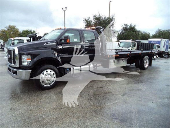 Ford F-750 tow truck with flatbed and crane, side view showing front chrome bumper and dual rear wheels.
