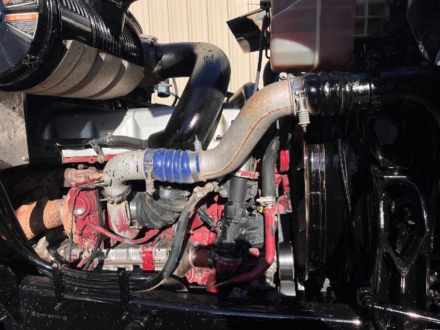 Mack CHU613 Pinnacle engine bay showing coolant hose, blue silicone hose, red engine components, and radiator fan, partial view of intake and belts.