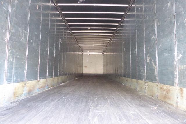 Trailer interior with empty cargo space, metal walls, wooden floor trim, overhead ceiling rails.