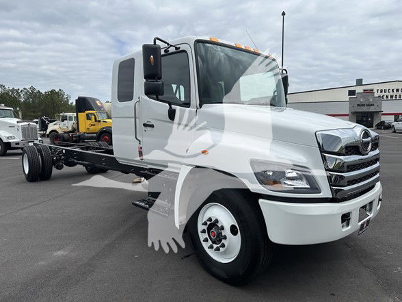 Front-right view of a white 2026 Hino L6 cab and chassis truck. Cab features large grille with Hino emblem, dual headlights, side mirrors, and amber clearance lights. No visible branding text aside from vehicle design.