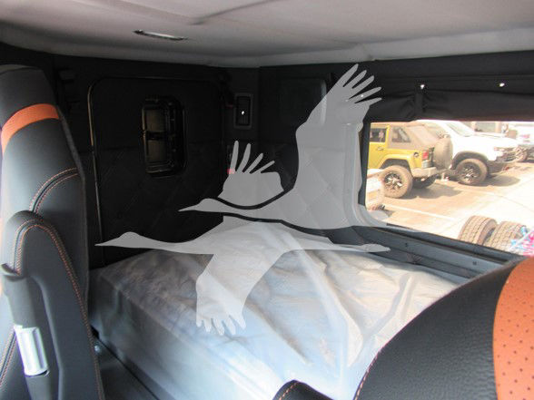 Kenworth W990 truck interior shows sleeping area with plastic-wrapped bed; windows and seating visible.