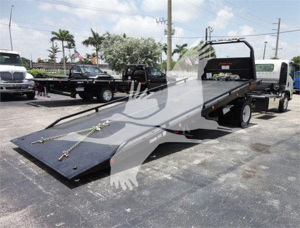 Isuzu flatbed tow truck with a long black steel deck and ramp, white cab, and rear wheel chocks visible.