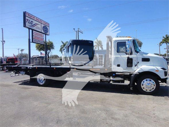 2024 Mack MD6 tow truck with a flatbed, white cab, long black flatbed, chrome wheels, dealership lot in background.
