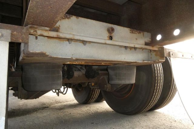 Trailer undercarriage showing dual rear axles with tires and rusted frame; undercarriage components visible.