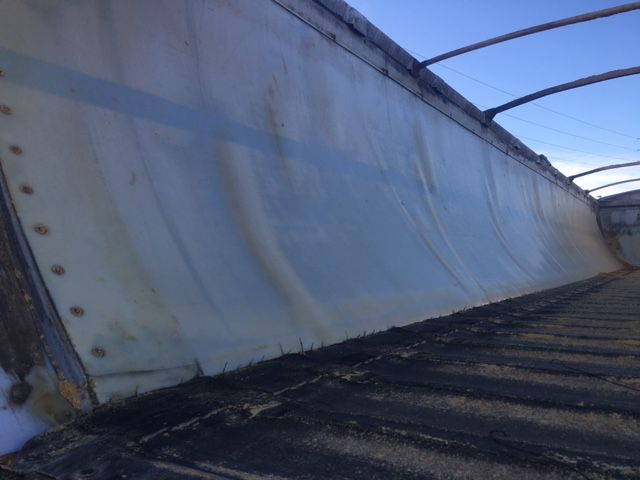 Trailer side with curved metal wall and black ribbed surface, showing riveted bolts and light blue paint.