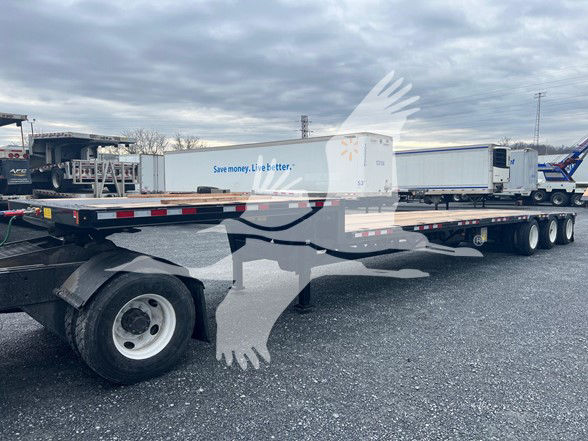 Side view of a 3-axle steel drop deck trailer with long flatbed and middle lift. Visible text on the trailer side reads 'Save money. Live better.' on the white trailer skin.