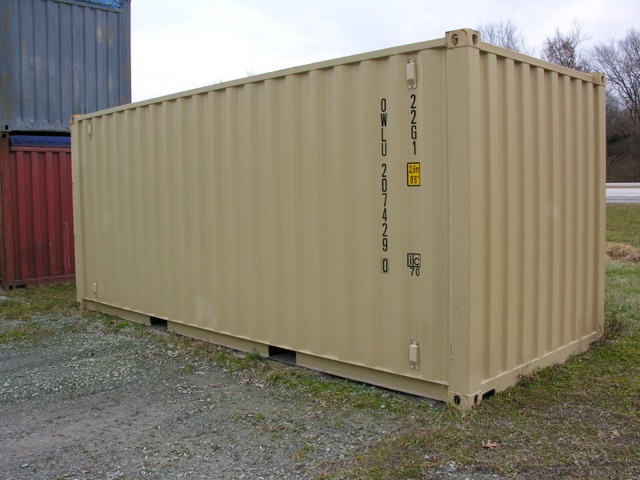Container trailer showing side with stamped codes and small yellow placard, beige color, on gravel lot.
