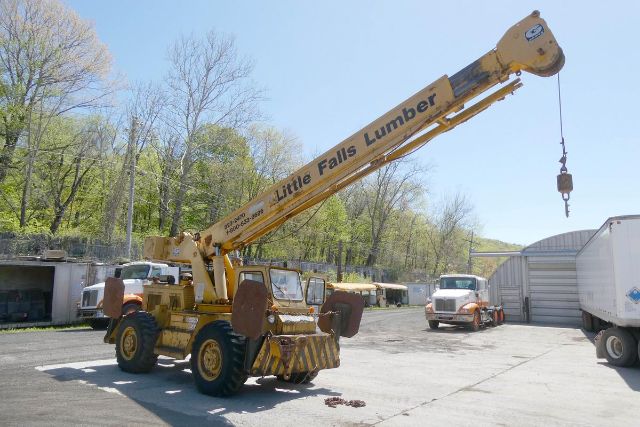 Grove RT58 crane truck in a yard with long yellow boom labeled 'Little Falls Lumber' and a hook at the end.