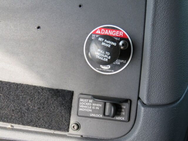 Capacitively lit circular caution label near dash and a lock switch with text must be locked when vehicle is in motion on Freightliner Cascadia Evolution truck interior