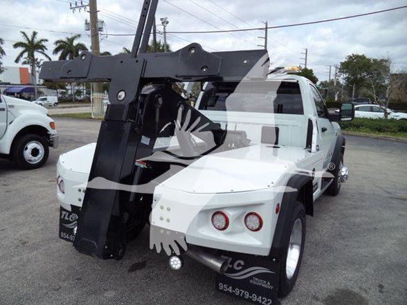 Ram tow truck rear view showing large hydraulic arm and winch, white cab and body, circular tail lights, black recovery apparatus.