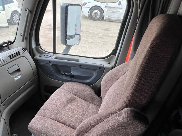 Truck cab interior showing driver's seat and door panel of a Freightliner Cascadia, side mirror visible through window.
