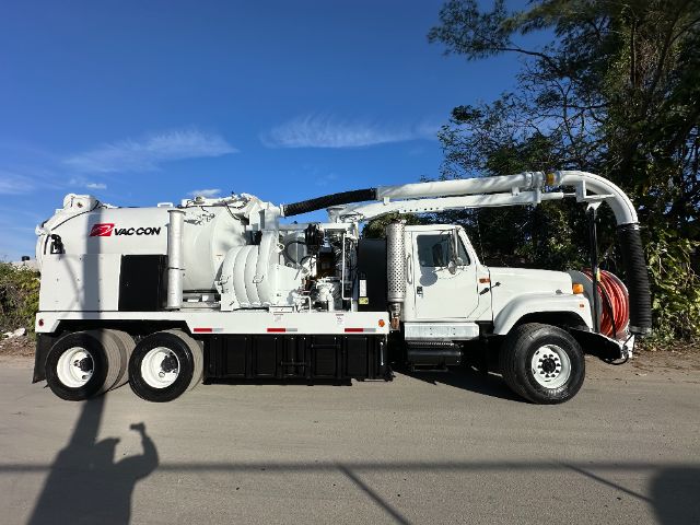 International F-2554 vacuum truck in side view with large white body, vacuum hose reel on side, and boom arm extended across top.