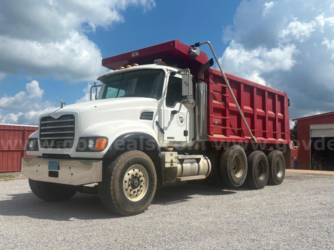 Mack CV713 dump truck with white cab and red dump bed, side view showing dual rear axles, chrome bumper, and large exhaust stack.