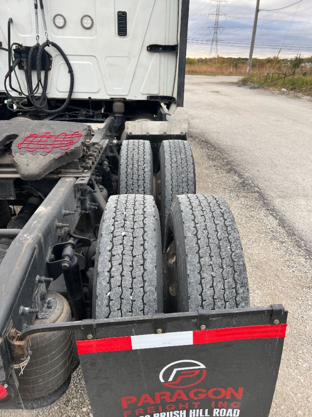 Trailer-axle view showing dual rear axles and mudguard with Paragon Freight logo; wheels and truck cab at left edge.