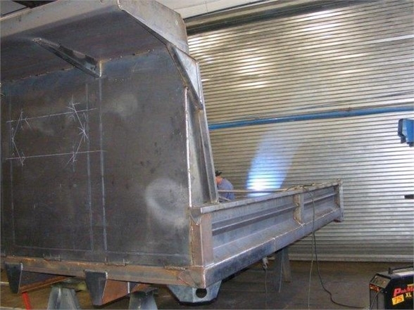 Dump body side and tail section of a 14 ft Advanced Fabricators dump truck bed in an indoor workshop with corrugated metal wall.