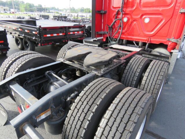 Truck chassis of a 2016 Freightliner Cascadia Evolution showing rear tandem axles, fifth wheel, and drivetrain components visible with red cab in background.