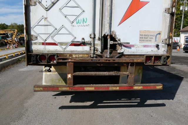 Rear of a trailer showing a metal bumper with rust and a rectangular cutout, taillights, and rear doors with diamond plate pattern.